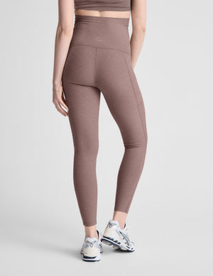 Woman wearing brown maternity leggings with pockets on a light gray background. 