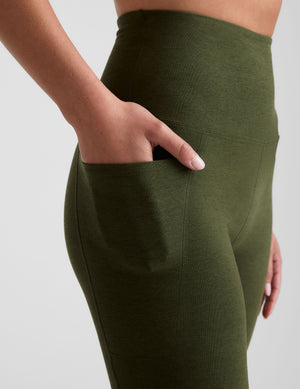 green high-waisted midi length leggings with side pockets on a plain background. 