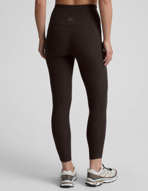woman wearing a brown high-waisted midi length pocket leggings  with a plain background. 