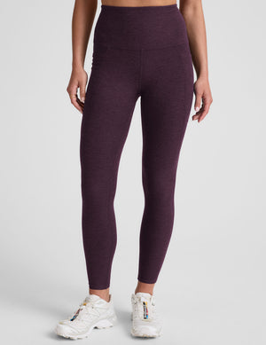 model wearing a purple t-shirt and purple high-waisted midi length leggings with pockets on a light gray background. 