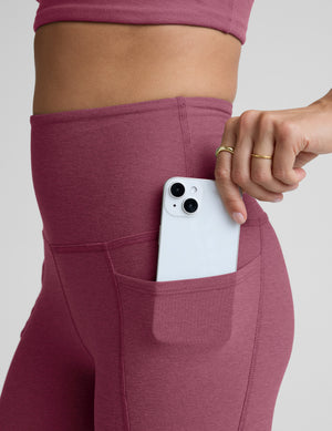 Person wearing purple leggings with a pocket holding a white phone on a plain background. 