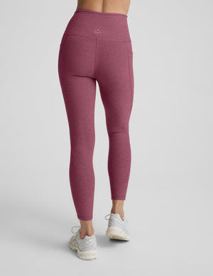Person wearing maroon leggings with a pockets against a plain background. 