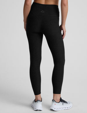 Black leggings with a front crossover waistband worn by a person on a light gray background. 