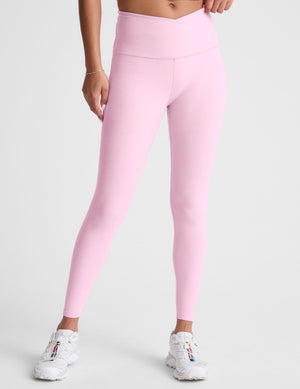 Woman wearing pink high-waisted midi leggings with a crossover waistband against a plain background. 