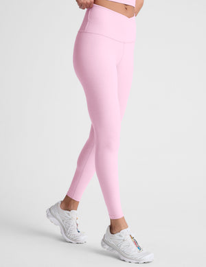 Woman wearing pink high-waisted midi leggings with a crossover waistband against a plain background. 