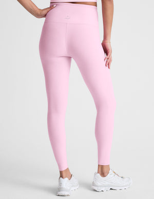Woman wearing pink high-waisted midi leggings with a crossover waistband against a plain background. 