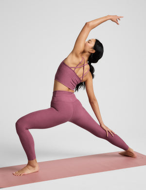 Woman in a yoga pose wearing a matching purple outfit on a white background. 