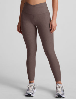 Brown leggings with a crossover front waistband worn by a person on a plain background. 