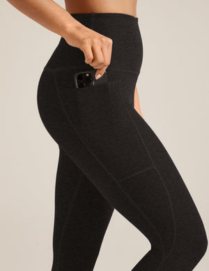 Side view of black marled Spacedye Out Of Pocket High Waisted Capri Legging featuring a hand placing a phone in a hip pocket.