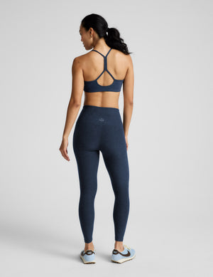 Woman wearing a navy blue sports bra and leggings set on a light gray background. 