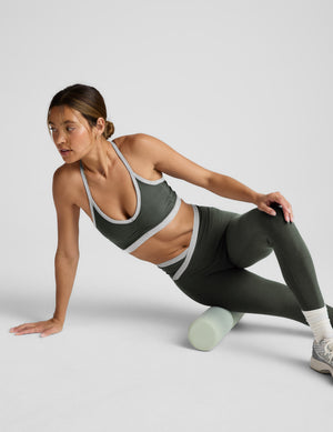 Woman in athletic wear using a foam roller on a light gray background. 