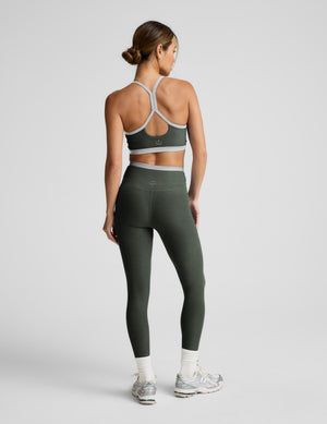 Woman wearing a green sports bra and leggings with gray accents on a plain background. 