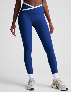 blue high-waisted midi length legging with a crossover detail on the front waistband with white contrast binding along waistline. 