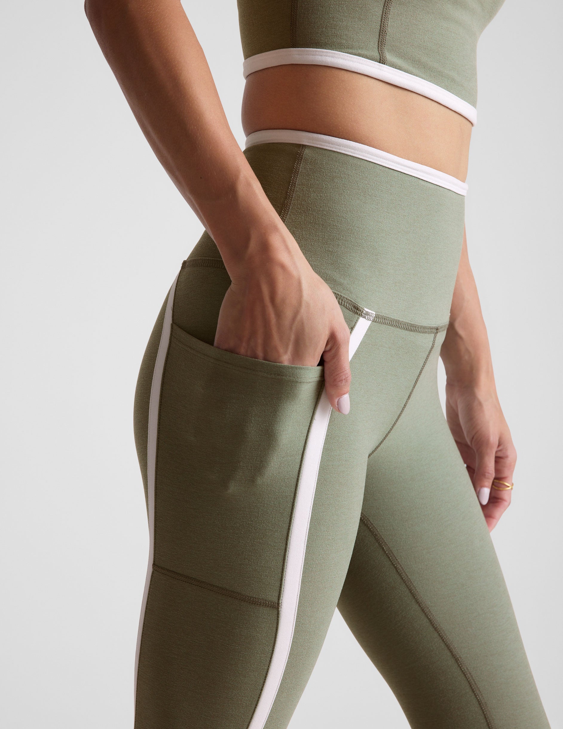 green high-waisted midi length legging with side pockets and white piping. 