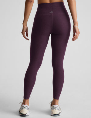Woman wearing purple midi length leggings with a drawcord at waistband on a gray background. 