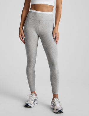 Person wearing gray leggings and white sneakers on a plain background. 