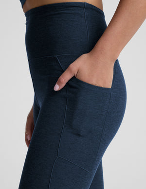 model wearing blue midi length leggings with 3 pockets against a plain background. 