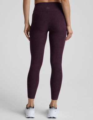 Woman wearing a purple high neck bra with mid-rise midi length leggings against a plain background. 