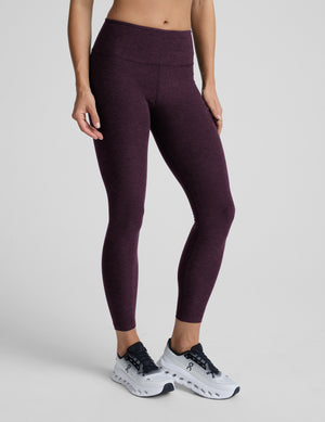 Woman wearing purple mid-rise midi length leggings on a light gray background. 