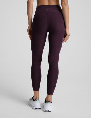 Woman wearing purple mid-rise midi length leggings on a light gray background. 
