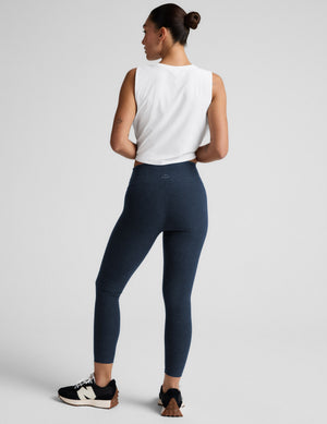 Woman wearing navy midi leggings and a white sleeveless top on a light gray background. 