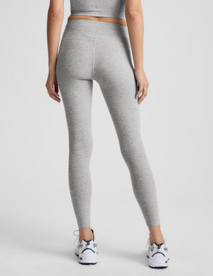 Woman wearing grey mid rise midi length leggings against a plain background. 