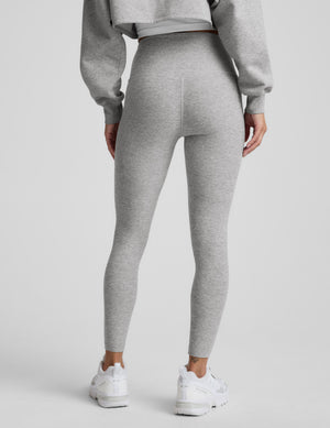 Woman wearing a gray sweatshirt and leggings set on a plain background. 