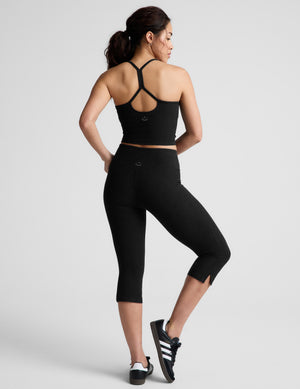 Back view of a model in black Spacedye Mid-Rise Slit Pedal Pusher Leggings with a mid-calf length and side hem slits.