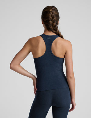 Woman wearing a navy blue tank top and leggings on a light gray background. 