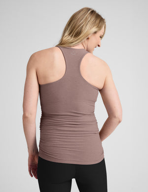 Pregnant woman wearing a brown tank top and black shorts on a light gray background. 