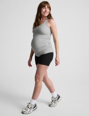 Woman wearing a gray maternity tank top and black shorts on a white background. 