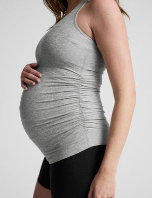 Woman wearing a gray maternity tank top and black shorts on a white background. 