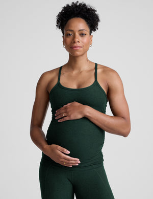 pregnant model wearing green maternity racerback tank top and green maternity leggings on a plain background. 