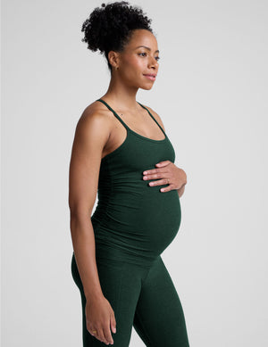 pregnant model wearing green maternity racerback tank top and green maternity leggings on a plain background. 