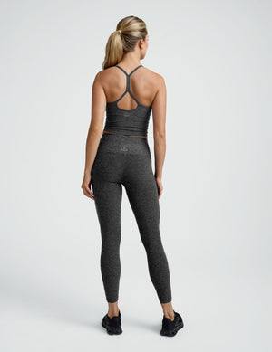 woman wearing a charcoal gray racerback cropped tank and leggings on a plain background. 