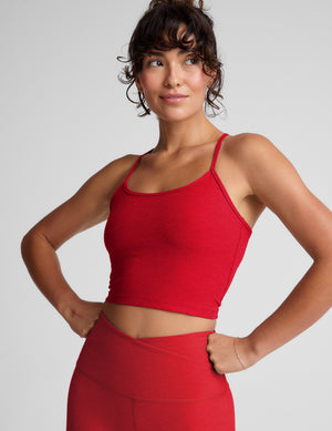 Woman wearing a red cropped tank and leggings on a plain background. 