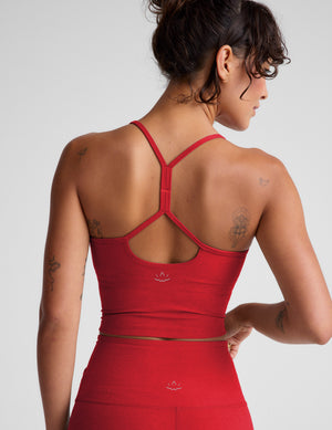 Woman wearing a red cropped tank and leggings on a plain background. 