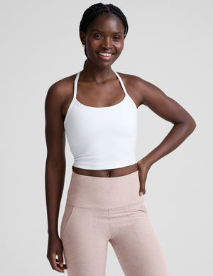 woman wearing a white racerback cropped tank and pink pants against a plain background. 