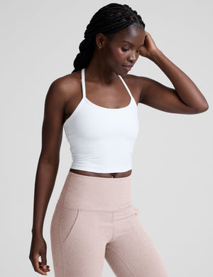 woman wearing a white racerback cropped tank and pink pants against a plain background. 