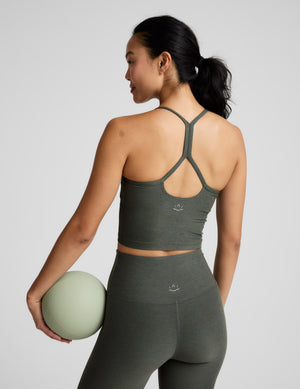 Woman wearing a green racerback cropped tank and leggings against a plain background. 