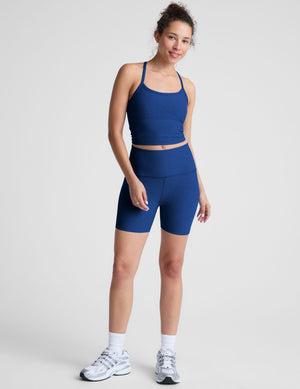 Woman wearing a blue racerback cropped tank against a plain background. 