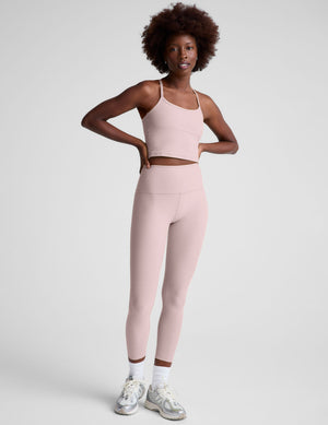 Woman wearing a pink racerback cropped tank and leggings on a light gray background. 