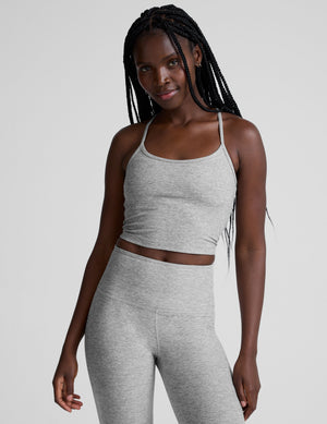 woman is wearing a gray racerback cropped tank and gray leggings against a plain background. 