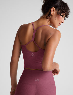 Woman wearing a purple racerback cropped tank and leggings against a plain background. 