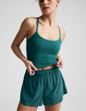 Woman wearing a green cropped tank and shorts against a plain background. 