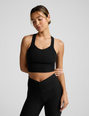 Woman wearing a black cropped tank with twist back details against a plain background. 