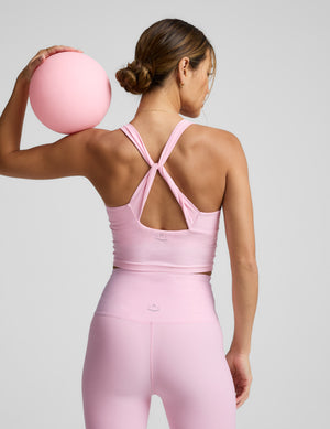 Woman wearing a pink cropped tank top with twist back strap details and leggings against a plain background. 
