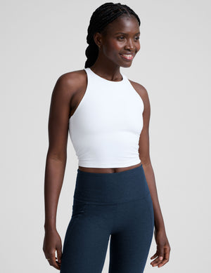 woman wearing a white high-neck racerback cropped tank and navy leggings on a plain background. 