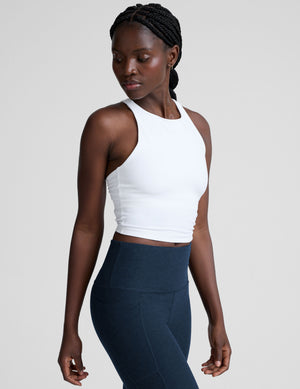woman wearing a white high-neck racerback cropped tank and navy leggings on a plain background. 