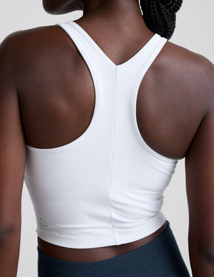 woman wearing a white high-neck racerback cropped tank and navy leggings on a plain background. 